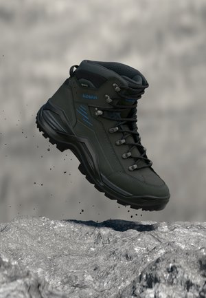 Bota de senderismo negra y azul con cordones flotando sobre una superficie rocosa, mostrando suela resistente y soporte acolchado para el tobillo.