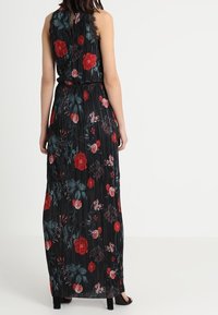 Robe maxi noire avec texture plissée et motif floral comportant des roses rouges et turquoises, et ceinture ajustable. Détail à col frangé.