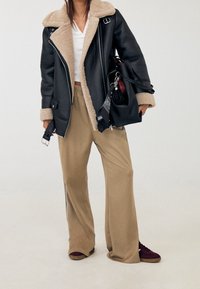 Schwarze Lederjacke mit beigem Lammfellfutter, beige weite Hosen und dunkelrote Sneaker. Enthält eine schwarze Handtasche mit dekorativer Beschläge.