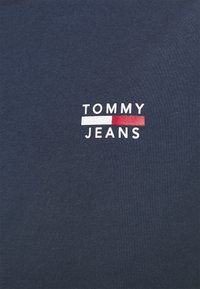 Marinblå bomullströja med vit logotext "TOMMY JEANS" och röda och vita horisontella ränder. Slät yta, korta ärmar.
