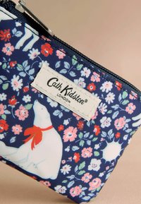 Tumesinine lilleline kott tõmbluku ja jääkaru illustratsiooniga, punase salliga ja Cath Kidstoni sildiga; sisaldab värvikirevaid lilli ja rohelisi lehti.