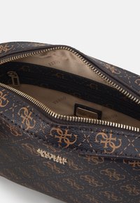 Interno di una borsa sintetica nera testurizzata con cerniera dorata, caratterizzato da un motivo logo in marrone chiaro e un piccolo tag del brand all'interno.