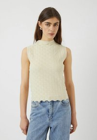 Top sin mangas color crema con un patrón texturizado y un dobladillo en forma de concha, combinado con jeans de mezclilla azul claro.