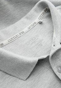 Grå bomullspikétröja med en texturerad yta, med klassisk krage, knappstängning och varumärkesetikett broderad i vitt innanför kragen.