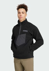 Pullover in pile nero con colletto mezzo zip, tasca sul petto grigia a contrasto e tessuto testurizzato. Presenta il logo del brand sul petto.