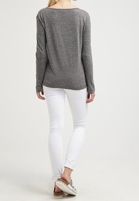 Maglietta grigia a maniche lunghe con una vestibilità comoda, abbinata a jeans skinny bianchi e scarpe slip-on argentate; tessuto morbido e dettagli minimi.