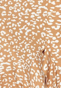 Tissu beige avec des taches irrégulières de léopard blanches et une texture subtile à côtes verticales sur un matériau plissé en couches.