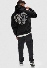Black hoodie with a large gray zebra-striped heart graphic on the back. Cotton blend with a relaxed fit and kangaroo pocket design.