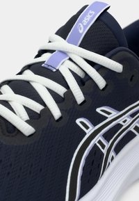 Ναυτικές αθλητικές παπούτσια με υφή στο επάνω μέρος, λευκά κορδόνια και μία διακριτική μοβ λεπτομέρεια. Διαθέτει μια καμπυλωτή λευκή και μαύρη σχεδίαση στο πλάι.