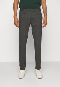 Szare spodnie chino o dopasowanym kroju, wykonane z tkaniny o fakturze, z zapięciem na guzik i bocznymi kieszeniami, zestawione z białymi sneakersami.