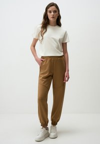 Lichtbeige T-shirt met korte mouwen, gecombineerd met bruine, slim fit joggingbroek met een elastische tailleband en cuffed ankles. Witte sneakers maken de look compleet.