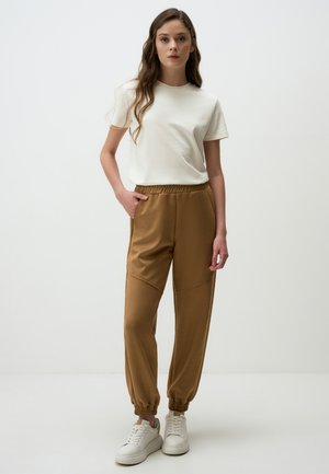 Lichtbeige T-shirt met korte mouwen, gecombineerd met bruine, slim fit joggingbroek met een elastische tailleband en cuffed ankles. Witte sneakers maken de look compleet.