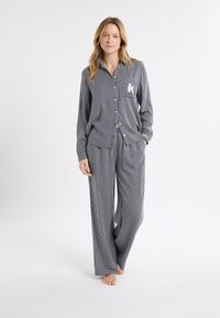 Niebiesko-biały piżamowy zestaw w paski, składający się z koszuli na guziki z kieszenią na piersi. Luźne spodnie z bocznymi kieszeniami, miękka tekstura tkaniny.