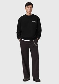 Felpa nera con collo rotondo e logo ricamato. Abbinata a pantaloni scuri con dettaglio a catena. Scarpe nere completano il look.