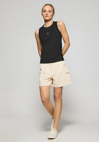 Czarna bezrękawnik z okrągłym dekoltem i logo z przodu, w zestawie z beżowymi szortami typu cargo z bocznymi kieszeniami i luźnym krojem.
