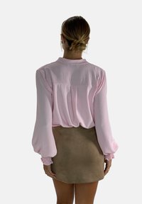 Lichtroze blouse met lange mouwen en kraag, van gemeleerd stof, met elastische manchetten en een ontspannen pasvorm, gecombineerd met een taupekleurige mini-jurk.