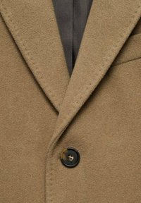 Manteau en laine marron avec un col cranté, un unique bouton noir et un tissu doux et texturé avec une doublure intérieure grise.