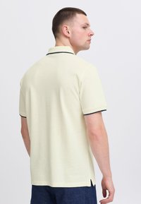 Kortermet polo med lys gul farge og marineblå detaljer på kragen. Har en rett kant og sideslister for en behagelig passform.