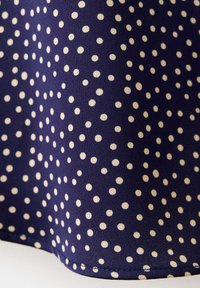 Tissu avec un fond bleu marine et des petits pois blancs répartis de manière régulière dans un motif répétitif.