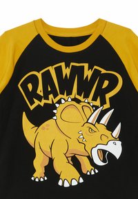 Mustapaita ja keltainen t-paita, jossa on keltainen dinosaurus, jossa on piikkejä, ja teksti "RAWR" paksuilla kirjaimilla.