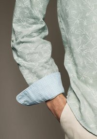 Grønt mønster skjorte med en struktureret stof, hvidt bambuslignende design; kontrasterende lyseblå manchet med et diamantmønster.