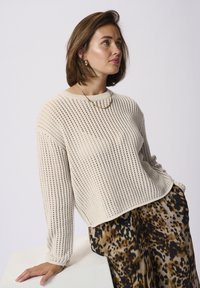 Pull en tricot de couleur crème, à la coupe ample, avec un tissage ouvert texturé. Associé à une jupe fluide à motif.