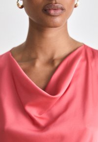 Ροζ μπλούζα με ζυγό λαιμό από απαλό ύφασμα, που διαθέτει μαλακά κρεμαστά και εφαρμοστή σιλουέτα γύρω από τον λαιμό και τους ώμους.