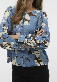 Bluse mit floralem Muster in Blau, Creme und Braun. Mit Puffärmeln, rundem Halsausschnitt mit Knöpfen und einem strukturierten Stoff mit großen Blumenmustern.