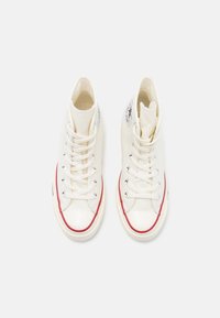 Paire de baskets montantes blanches en toile avec une bande rouge autour de la semelle et un logo étoile noire sur la cheville intérieure, vue de dessus.