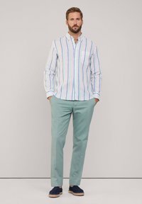 Gestreept button-down shirt met pasteltinten op een witte achtergrond, gecombineerd met lichtgroene broek en donkerblauwe espadrilles.