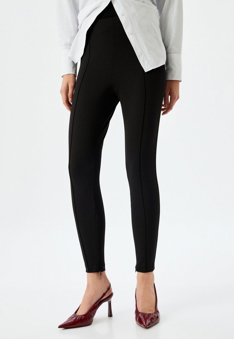 Leggings neri con un design aderente, caratterizzati da cuciture laterali e una texture liscia. Abbinati a tacchi a punta bordeaux.