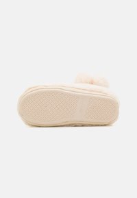 Light pink slipper with plush upper, rounded shape, two pom-poms on the front, and textured rubber sole for grip.