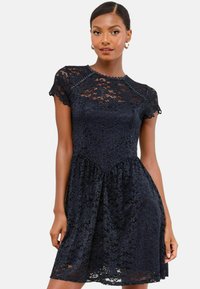 Rochie bleumarin din dantelă cu mâneci scurte, model floral, decolteu cu margini ondulate, corset ajustat și fustă evazată, evidențiind detalii complicate.