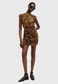 Robe à imprimé léopard avec des épaules volantes, une texture froncée et une silhouette ajustée. Associée à des chaussures à brides à la cheville noires. Des lunettes de soleil noires complètent le look.