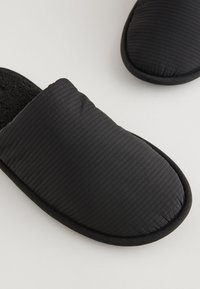 Chaussons noirs sans lacets avec texture côtelée, dessus rembourré et doublure douce. Conception à bout arrondi et bordure contrastante le long du bord.