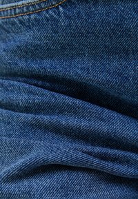 Tela vaquera, color azul profundo, con una textura suave y variaciones sutiles, doblada con costuras visibles.