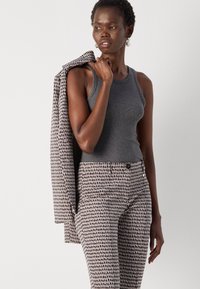 Grauer ärmelloser Pullover aus Strickstoff, kombiniert mit gemusterten, taillierten Hosen mit Punkten in Beige- und Brauntönen, getragen mit einem Blazer.