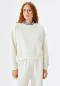 Crème-kleurige sweatshirt van zachte stof, met een ronde hals, verlaagde schouders en ribgebreide manchetten. Gecombineerd met bijpassende lichtgekleurde broek.