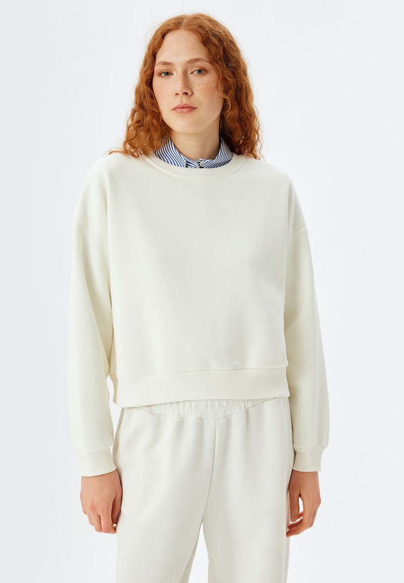 Crème-kleurige sweatshirt van zachte stof, met een ronde hals, verlaagde schouders en ribgebreide manchetten. Gecombineerd met bijpassende lichtgekleurde broek.