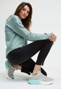 Light blue sweatshirt, black jeans with bead accents, and gray sneakers featuring a mint green sole and detailing.