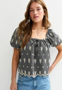 Black and white checked blouse with puff sleeves, floral embroidery, and a scalloped lace hem. Lightweight fabric with a relaxed fit.