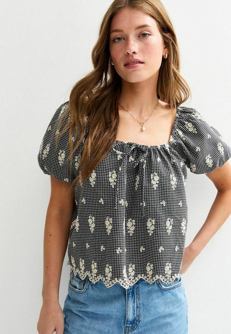 Blusa a cuadros en blanco y negro con mangas abullonadas, bordado floral y dobladillo de encaje con forma de ondas. Tejido liviano con un corte holgado.