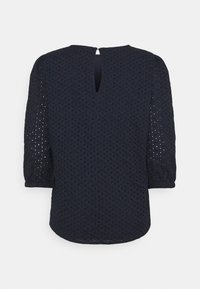 Haut bleu marine avec un motif texturé et des manches trois-quarts. Le dos présente une ouverture en forme de trou avec un détail de bouton. Tissu léger.