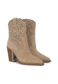 Botines de ante beige con punta afilada y tacón apilado. Presentan tachuelas decorativas y gemas en un patrón floral. Cierre de cremallera en la parte trasera.