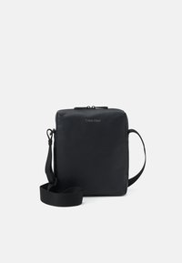 Borsa a tracolla nera realizzata in pelle texture con forma quadrata. Dotata di chiusura a zip e tracolla removibile. Design minimalista con logo.