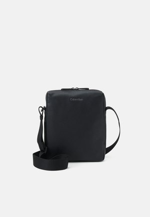 Borsa a tracolla nera realizzata in pelle texture con forma quadrata. Dotata di chiusura a zip e tracolla removibile. Design minimalista con logo.