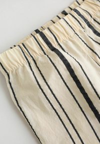 Shorts en tissu de coton avec une ceinture élastique, présentant des rayures verticales noires sur un fond pâle. Texture douce et design décontracté.