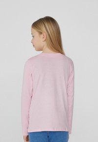 Różowa bluzka z długim rękawem z miękkiego materiału, z okrągłym dekoltem i detalem szwu z tyłu, w połączeniu z niebieskimi dżinsami.