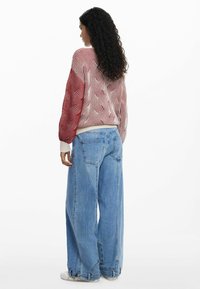 Rot-weiß gemusterter Pullover mit Ballonärmeln, kombiniert mit weit geschnittenen blauen Jeans. Weiche Textur mit gerippten Bündchen und Saum.