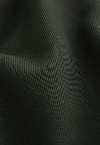 Tessuto testurizzato di colore verde scuro, con un motivo intrecciato e una sottile lucentezza, caratterizzato da una sensazione morbida e liscia. Ideale per abbigliamento o rivestimenti.